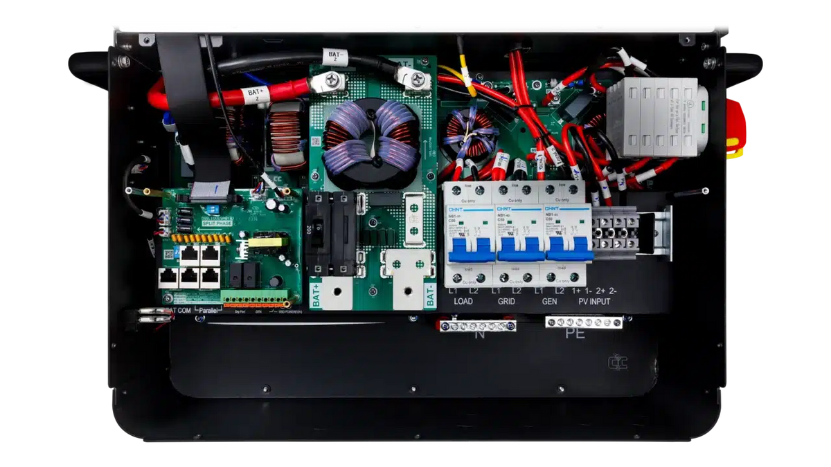 An open BigBattery electrical control box displays organized circuit boards, wiring, fuses, switches, breakers, and clearly labeled ports for input, grid, and load connections. All components are arranged for easy access and maintenance. The labels—presented in a highly legible IBM Plex Sans font—ensure optimal readability throughout the control box.