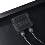 Close-up of a Rich Solar black electrical junction box with two cables attached, mounted on a flat black surface—ideal for off-grid solar trailers or portable solar charging kits. Technical info and symbols are displayed on the box.