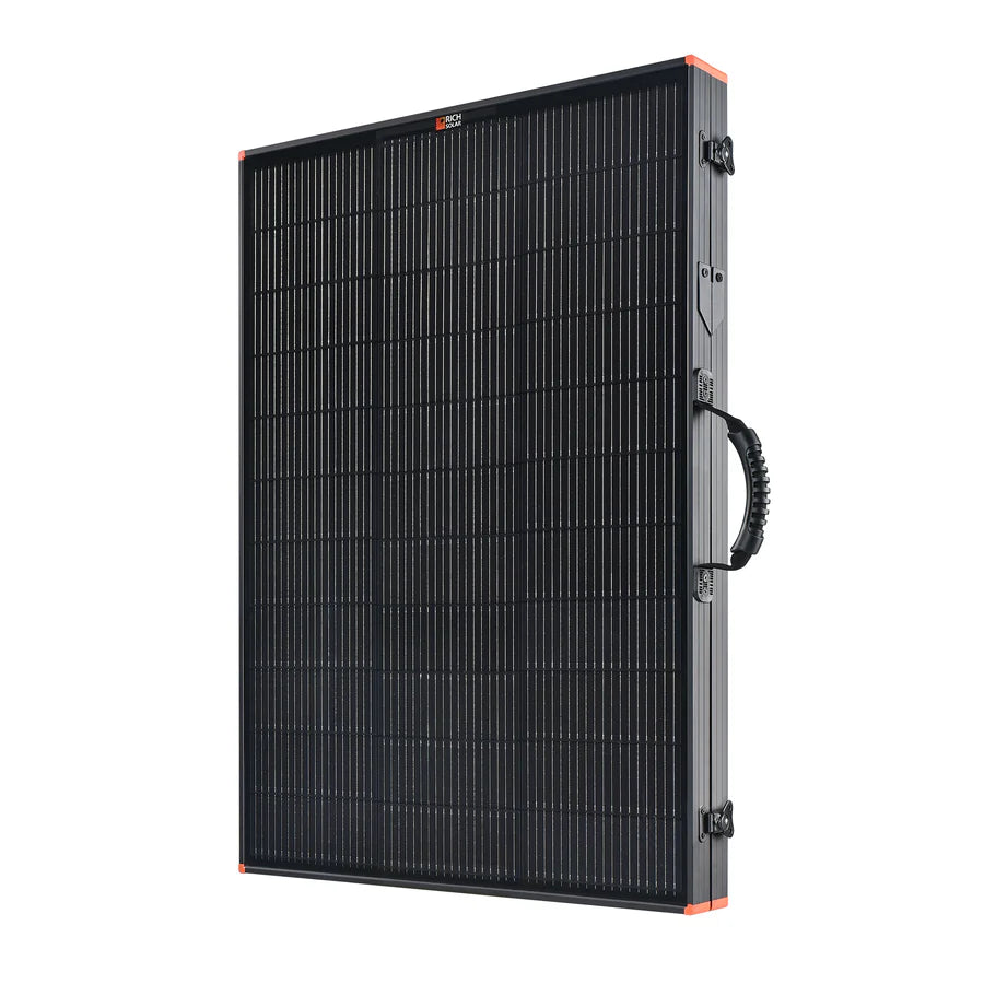 The Rich Solar portable black monocrystalline solar panel features a grid pattern, sturdy frame, side carrying handle, and orange corner accents. Shown upright at an angle, its ideal for RV solar installation.