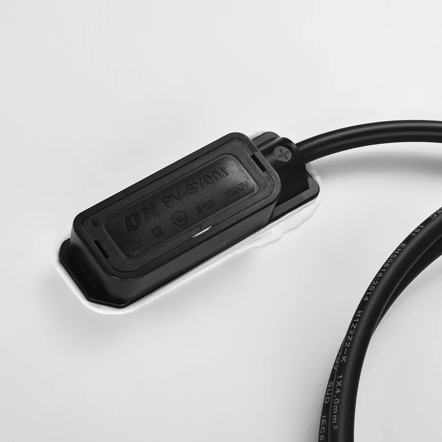 A black rectangular junction box labeled QX PVS7601, featuring subtle box-shadow effects, is attached to a black cable and rests on a white surface.
